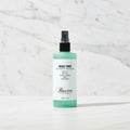 A bottle of Baxter of California Shave Tonic with a mint green and white label, black spray top, and clear cap, shown on a plain white background.