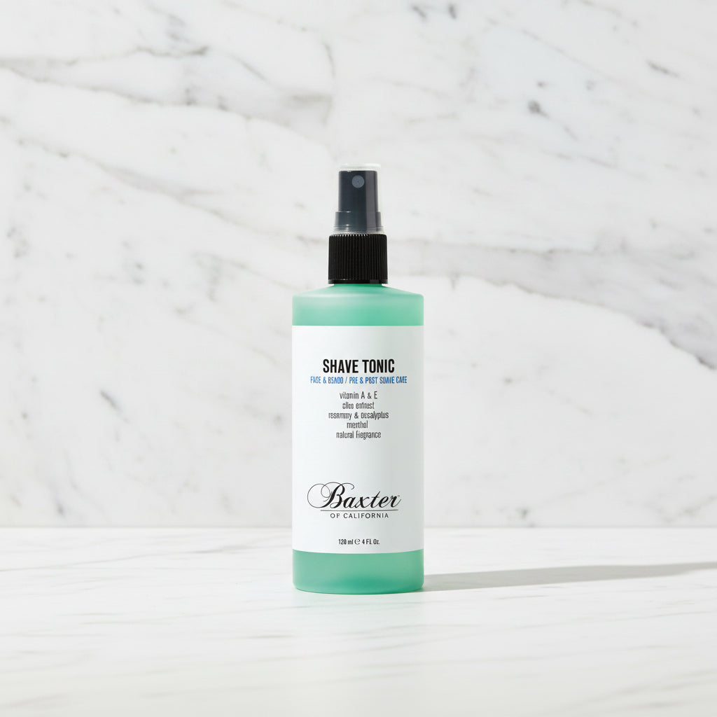A bottle of Baxter of California Shave Tonic with a mint green and white label, black spray top, and clear cap, shown on a plain white background.
