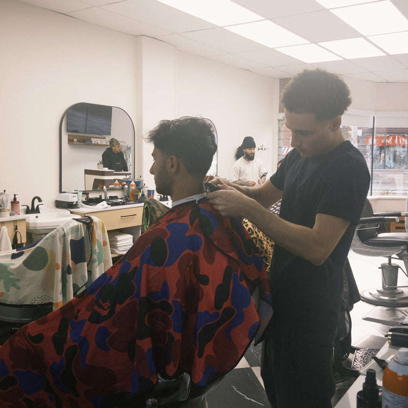 Barber cutting a customer's hair with a colorful cape in a salon.